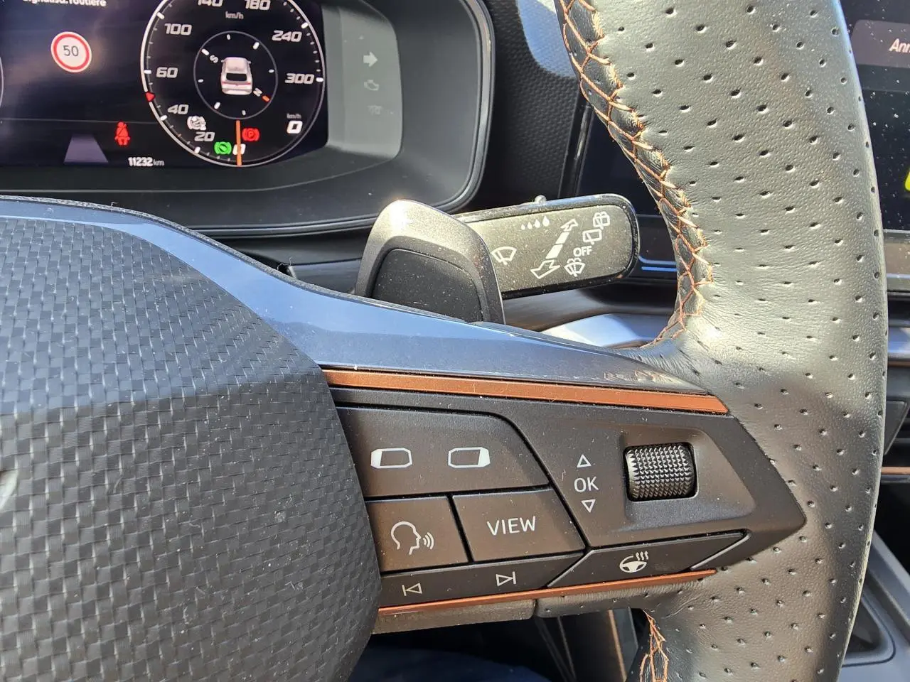 Gros plan sur les commandes du volant cuir perforé avec surpiqûres marron du CUPRA Leon Sportstourer blanc Nevada 2024.