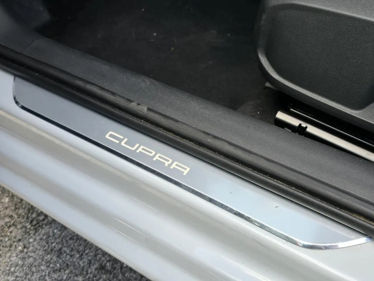 Gros plan sur la plaque de seuil de porte illuminée Cupra, sur fond de carrosserie blanc Nevada métallisé.