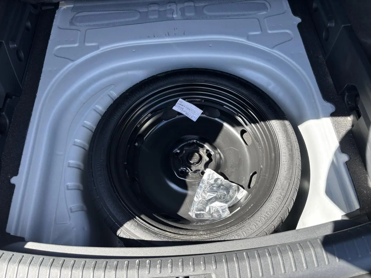 Vue plongeante sur la roue de secours noire dans le coffre blanc Nevada d'une CUPRA Leon Sportstourer 2024.