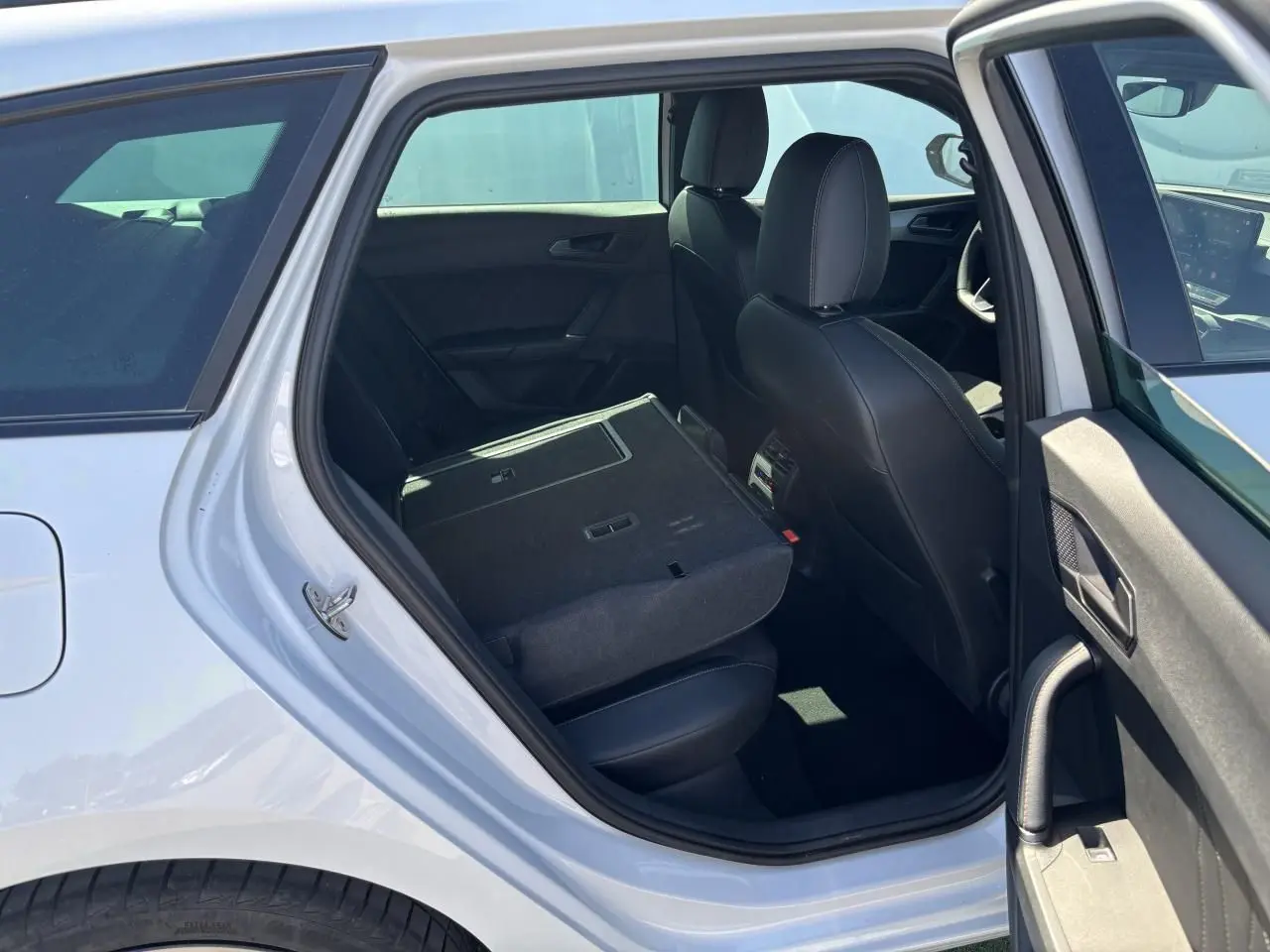 Vue intérieure côté gauche arrière de la CUPRA Leon Sportstourer blanche avec banquette rabattue et sièges noirs en cuir.
