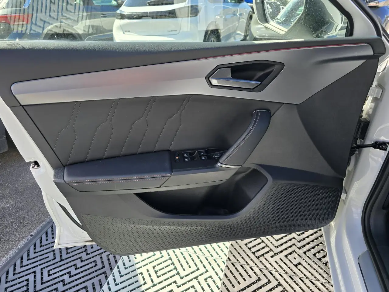 Vue rapprochée de la porte avant gauche blanche Nevada du CUPRA Leon Sportstourer avec garniture noire et surpiqûres contrastées.