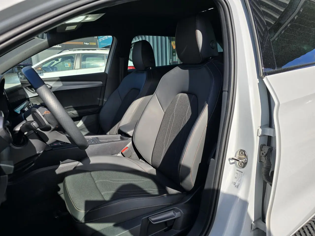 Vue intérieure côté conducteur d'une CUPRA Leon Sportstourer blanche Nevada, sièges sport en cuir et tissu noir.