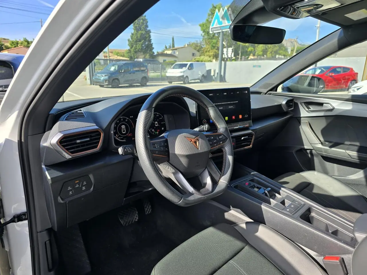 Vue intérieure côté conducteur du CUPRA Leon blanc Nevada, avec volant sport, écran tactile HD et tableau de bord digital.