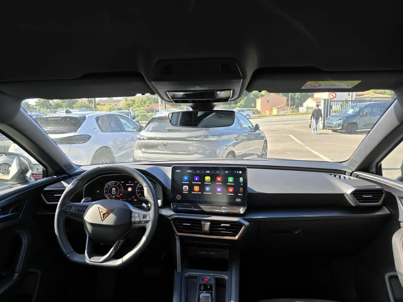 Vue intérieure du tableau de bord et volant Cupra d'une Leon Sportstourer 2024, avec écran tactile central allumé.