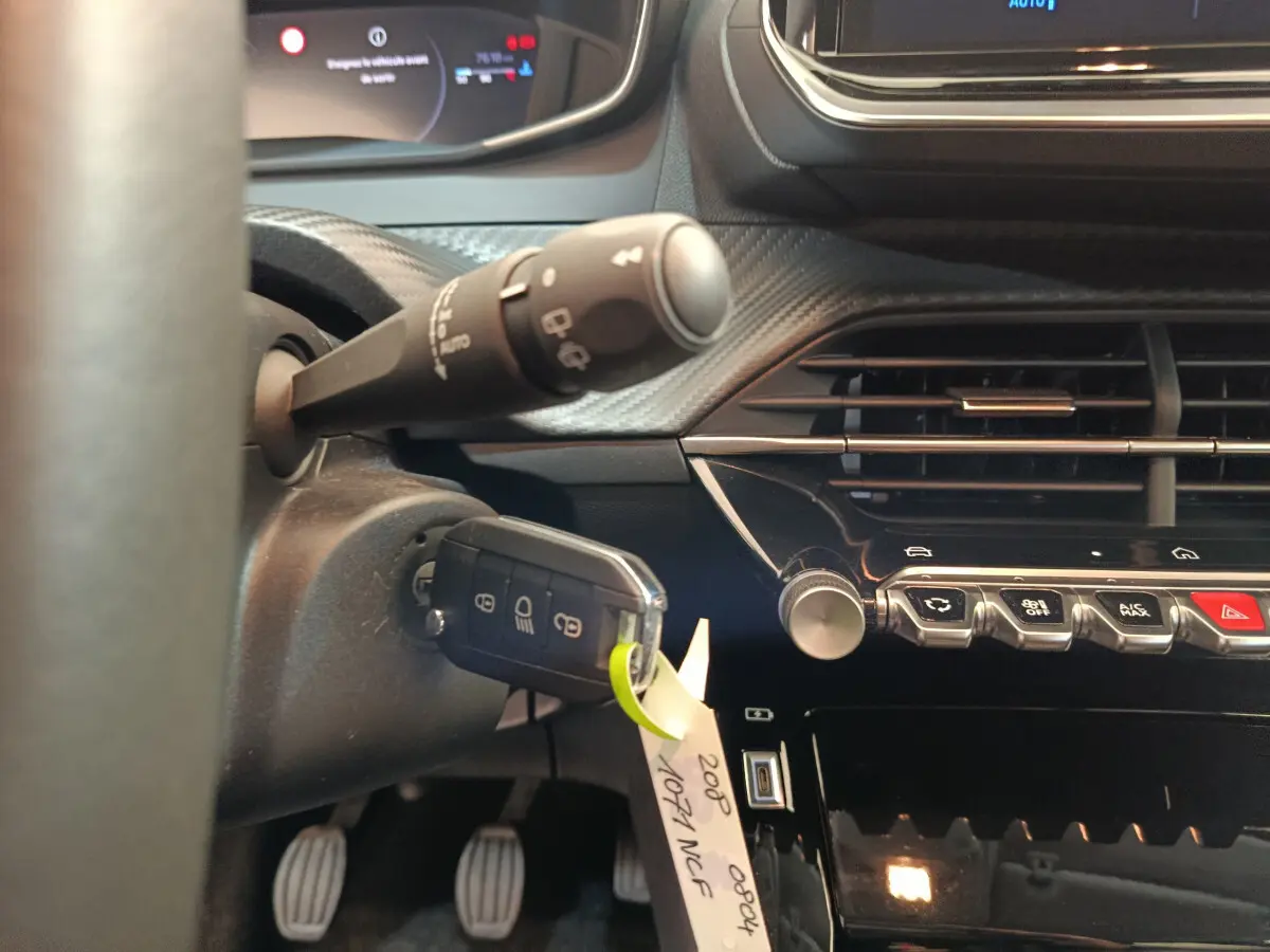 Vue intérieure rapprochée du tableau de bord et du volant de la Peugeot 208 gris clair, avec clé insérée et commandes visibles.