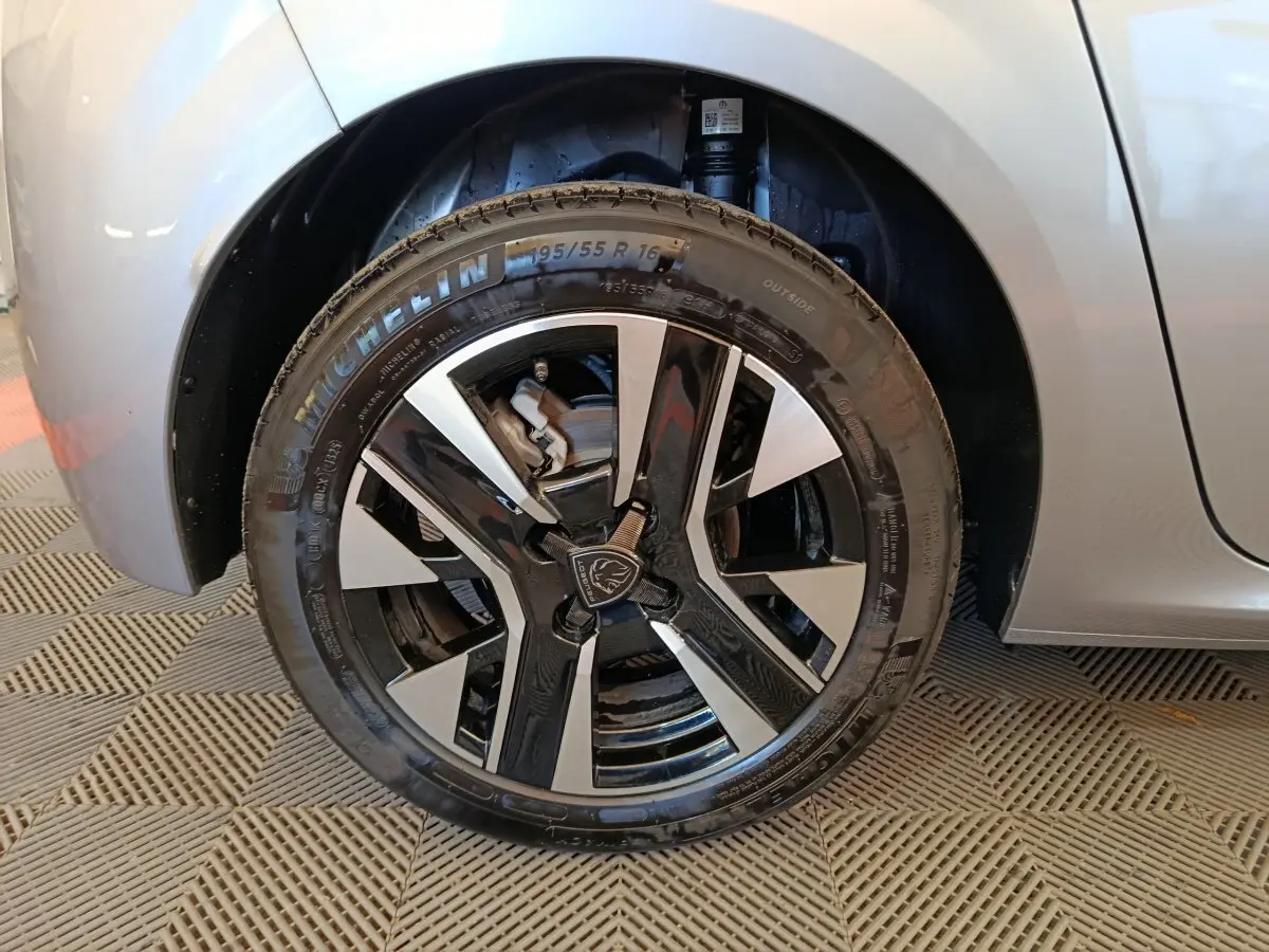 Gros plan sur la roue avant gauche gris clair de la Peugeot 208 PureTech 100 S&S Allure avec jante alliage bicolore.