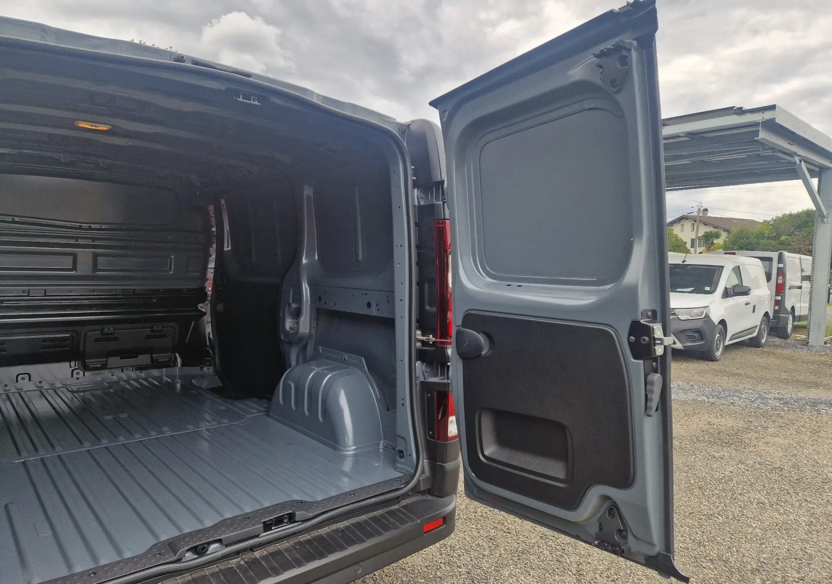 Vue arrière ouverte du Renault Trafic Fourgon gris urbain 2025, montrant l’espace de chargement vide et la porte battante droite ouverte.