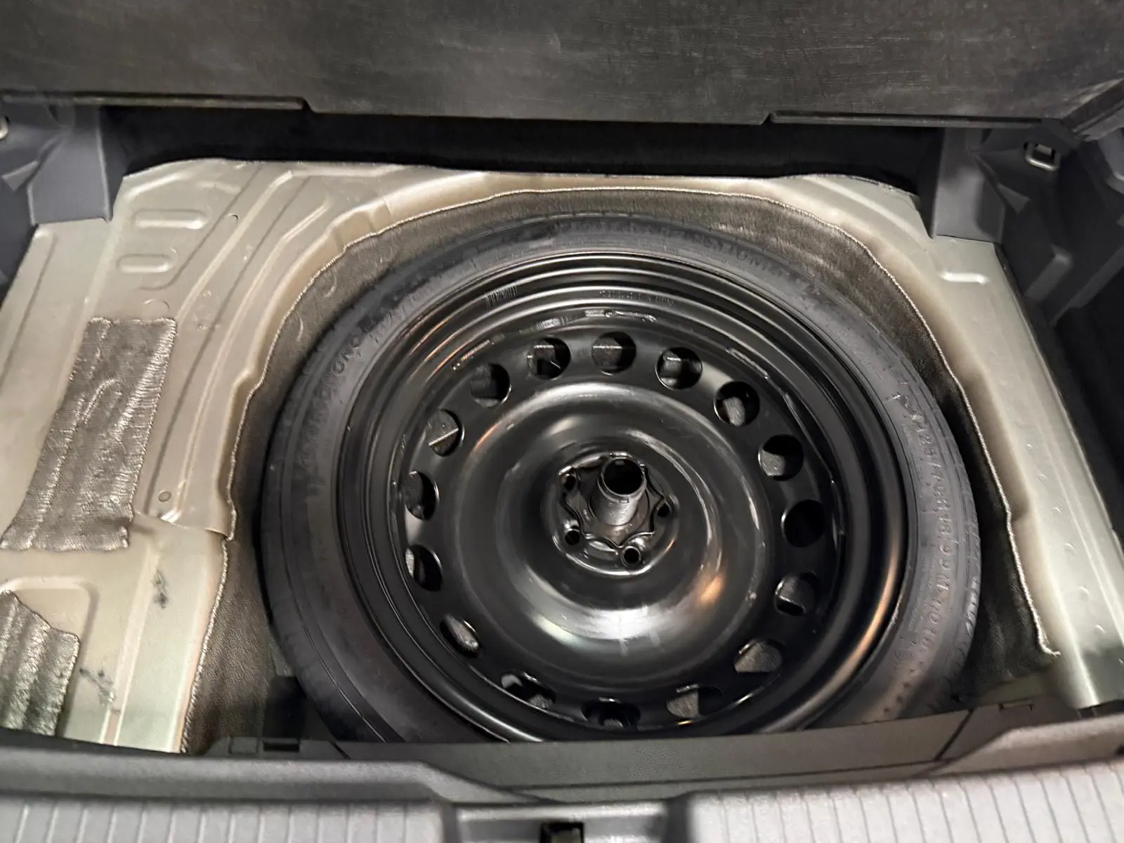 Gros plan sur la roue de secours compacte noire dans le coffre du Volkswagen T-Cross 2024 couleur Reflet d'Argent.