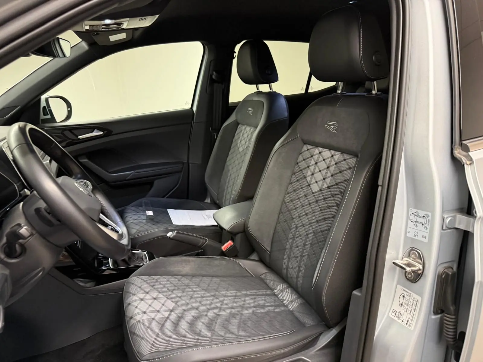 Vue intérieure côté conducteur du Volkswagen T-Cross 1.5 TSI R-Line 2024, sièges avant noirs avec surpiqûres et logo R-Line.