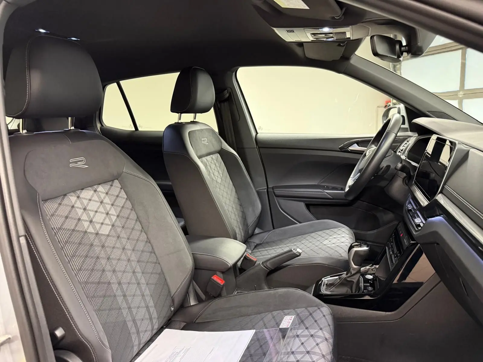 Vue intérieure côté conducteur du Volkswagen T-Cross 1.5 TSI R-Line 2024, sièges noirs avec surpiqûres et logo R brodé.