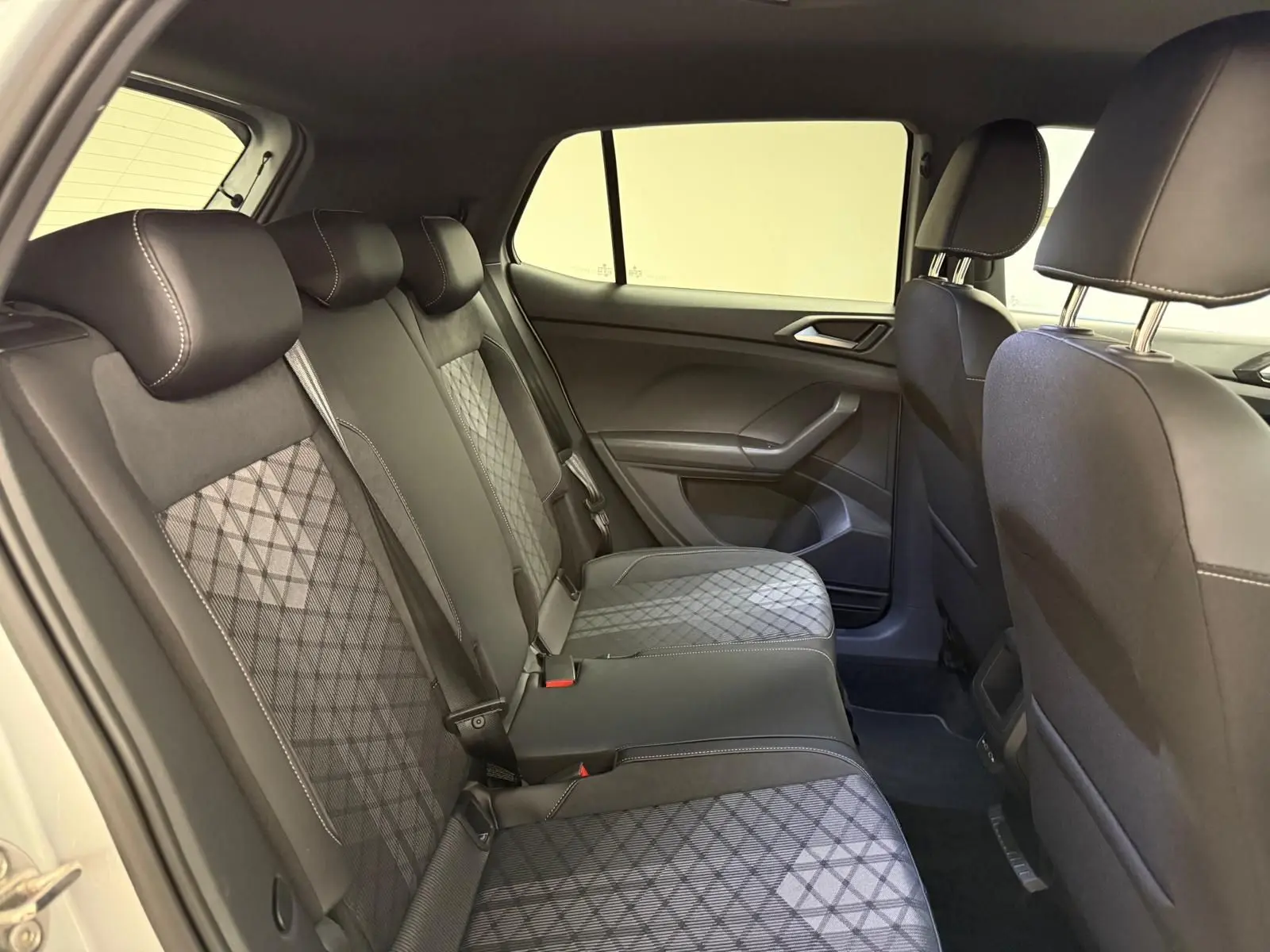 Vue intérieure côté droit de la banquette arrière du Volkswagen T-Cross 2024 avec sièges en tissu noir à motifs géométriques.