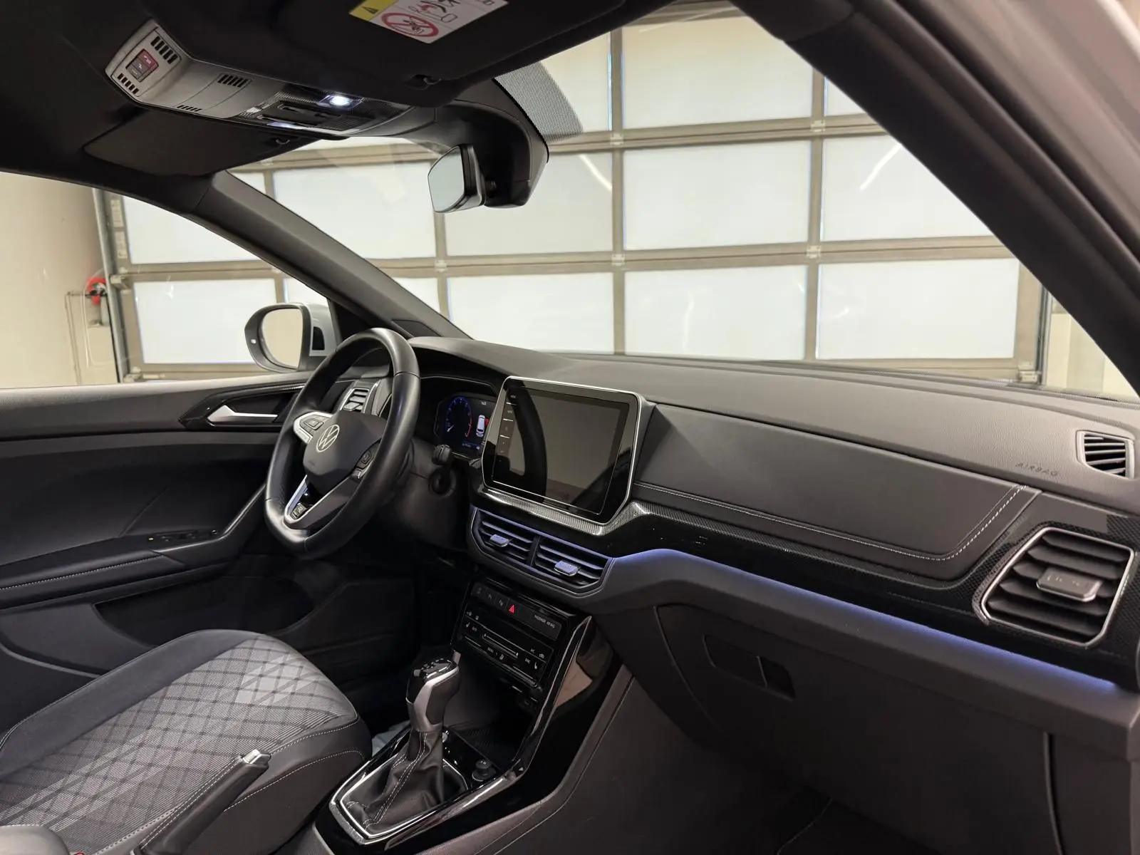 Vue intérieure côté conducteur du Volkswagen T-Cross 2024, tableau de bord noir avec écran tactile central et volant multifonction.