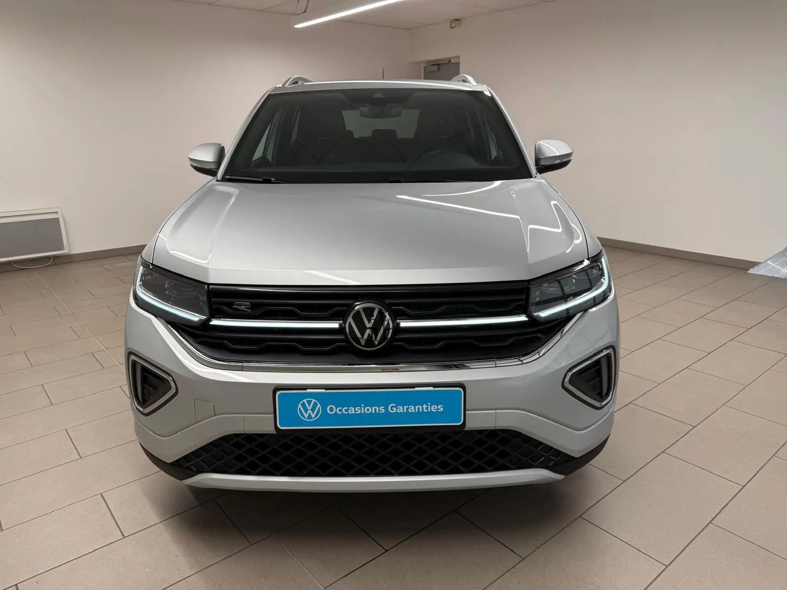 Vue frontale d'un Volkswagen T-Cross 1.5 TSI 150 DSG7 R-Line en peinture métallisée Reflet d'Argent, intérieur showroom.