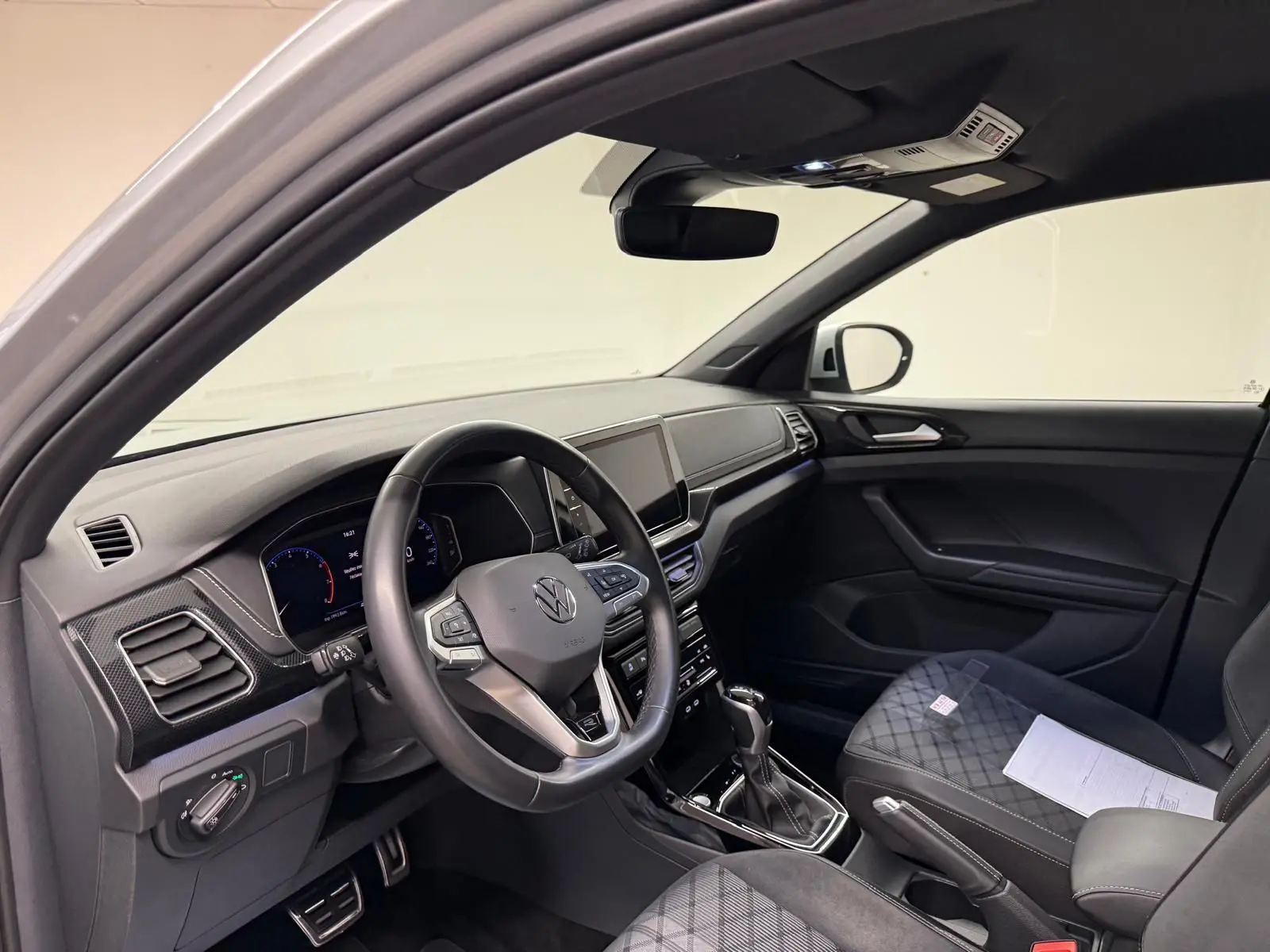 Vue intérieure côté conducteur du Volkswagen T-Cross 1.5 TSI R-Line 2024, tableau de bord et sièges noirs avec surpiqûres.