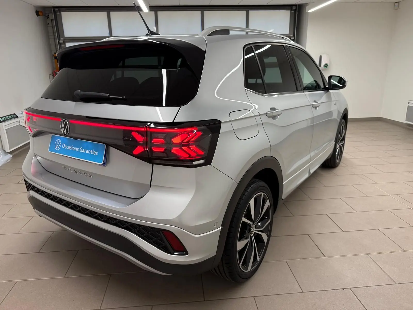 Vue 3/4 arrière droite du Volkswagen T-Cross 1.5 TSI R-Line 2024 en peinture métallisée Reflet d'Argent avec feux arrière LED allumés.