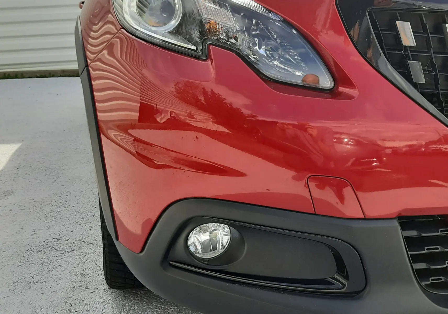 Gros plan sur l'avant droit rouge Ultimate Metal du Peugeot 2008 GT Line, mettant en valeur le phare et le antibrouillard.