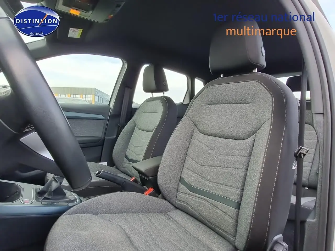 Vue intérieure côté conducteur du SEAT Arona 2023, montrant les sièges gris et l'accoudoir central avec levier de vitesse manuel.