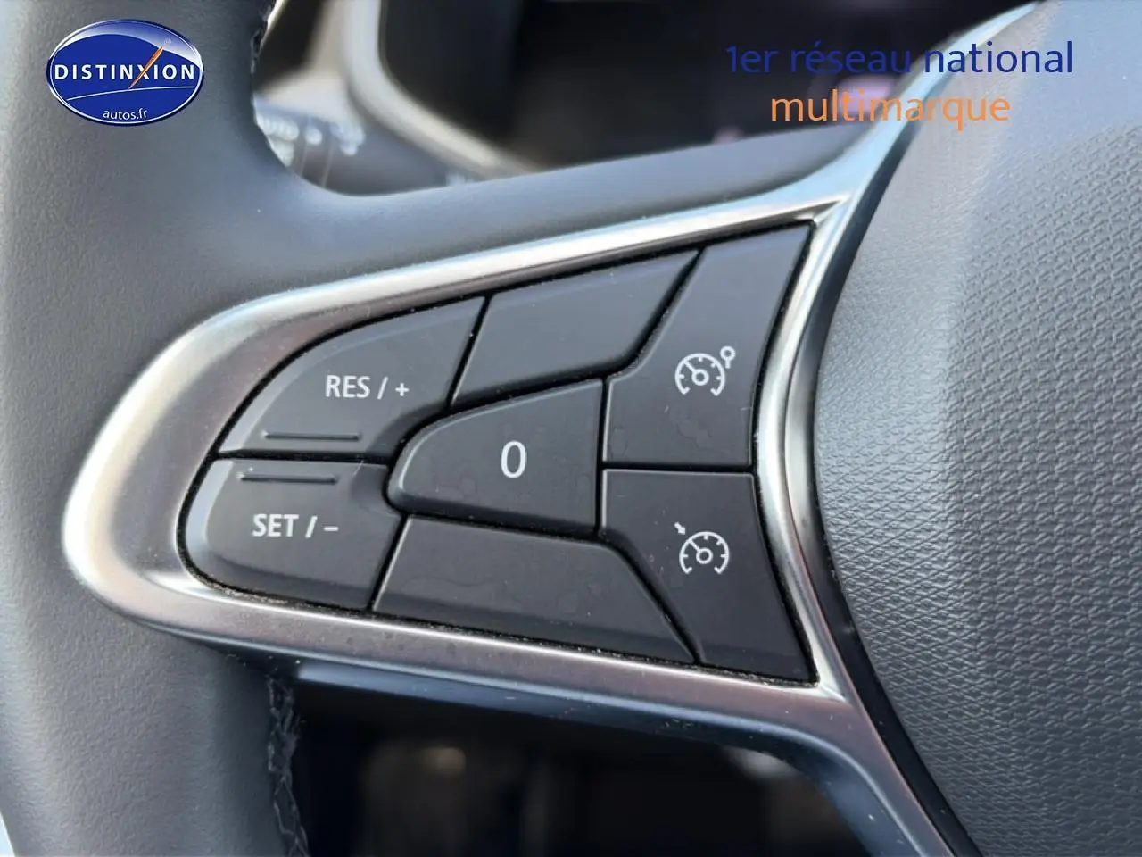 Gros plan sur les commandes de régulateur de vitesse au volant d'une Renault Clio V gris foncé.