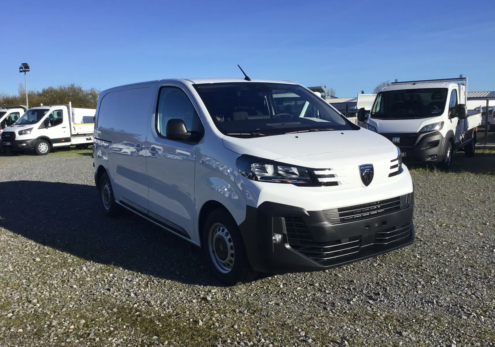 Vue 3/4 avant d'un Peugeot Expert Fourgon blanc 2024 avec calandre noire et jantes acier sur parking.