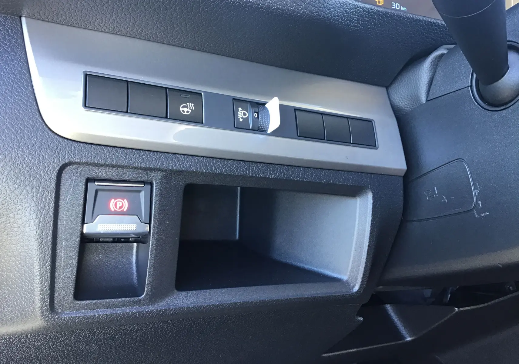 Gros plan sur le tableau de bord côté gauche du Peugeot Expert Fourgon blanc 2024, avec bouton frein à main électronique et réglage des phares.