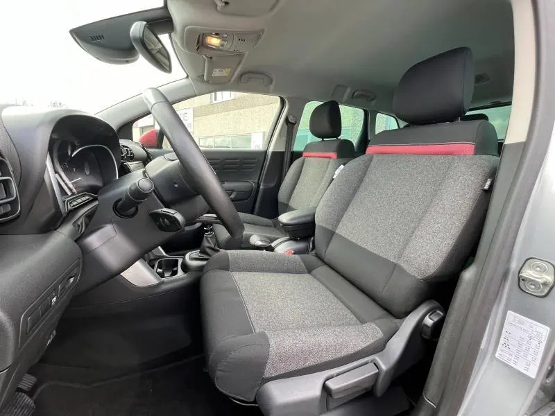 Intérieur avant droit du Citroën C3 Aircross gris acier, sièges tissu gris avec bande rouge et volant cuir.