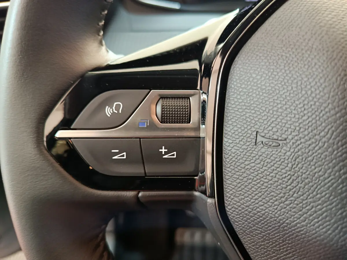 Gros plan sur les commandes gauche du volant noir de la Peugeot 208 PureTech 100 S&S Allure 2025.