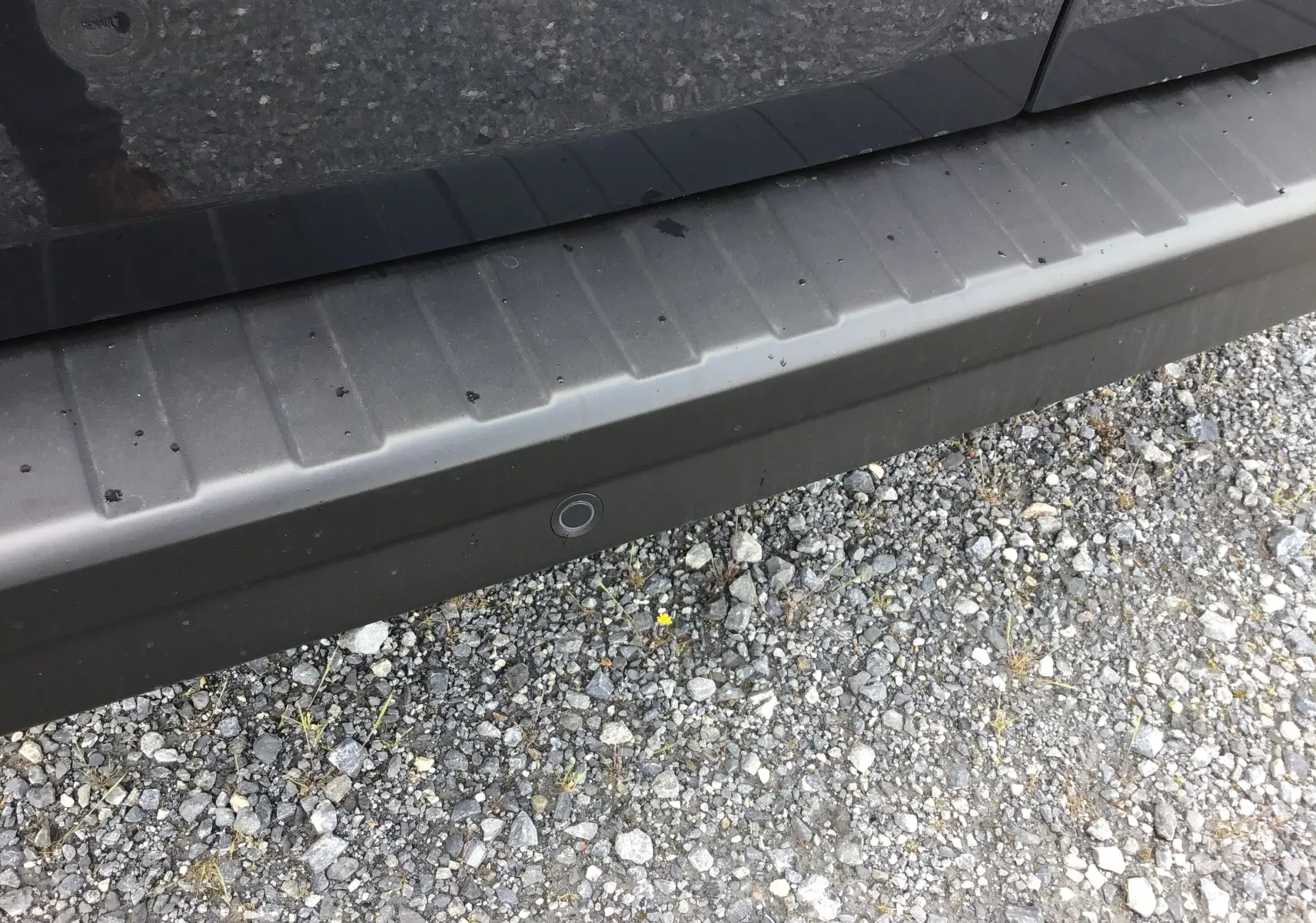 Gros plan sur le bas de porte gris comète du Renault Trafic Fourgon, avec capteur de recul visible sur le pare-chocs.