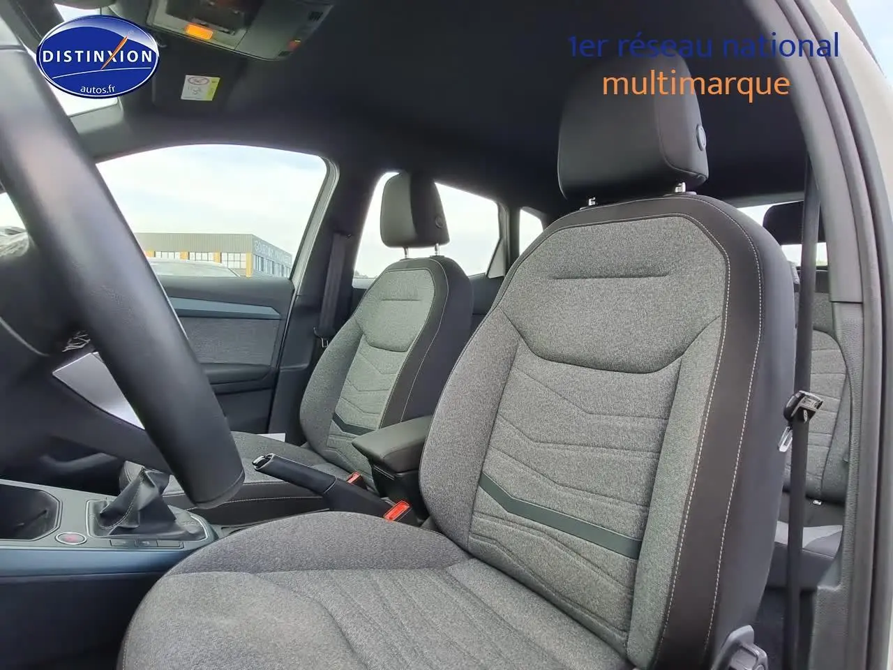 Intérieur du SEAT Arona 2023 essence, vue côté conducteur sur sièges gris tissu avec accoudoir central noir.