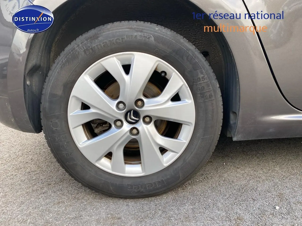 Gros plan sur la roue avant gauche d'une Citroën C4 Picasso gris métallisé avec jante alu et logo Citroën visible.