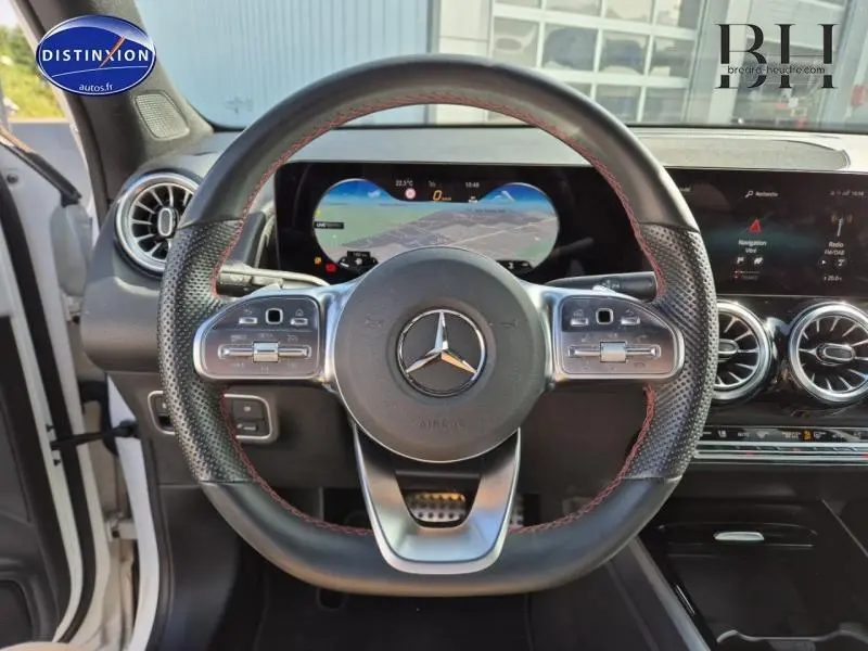 Vue rapprochée du volant cuir noir avec surpiqûres rouges du Mercedes GLB 200 d AMG Line 2023, tableau de bord digital visible.