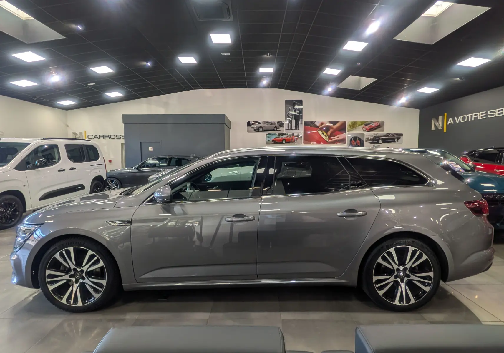 Profil côté gauche d'une Renault Talisman Estate gris Cassiopé, break élégant avec jantes alliage bicolores en showroom.