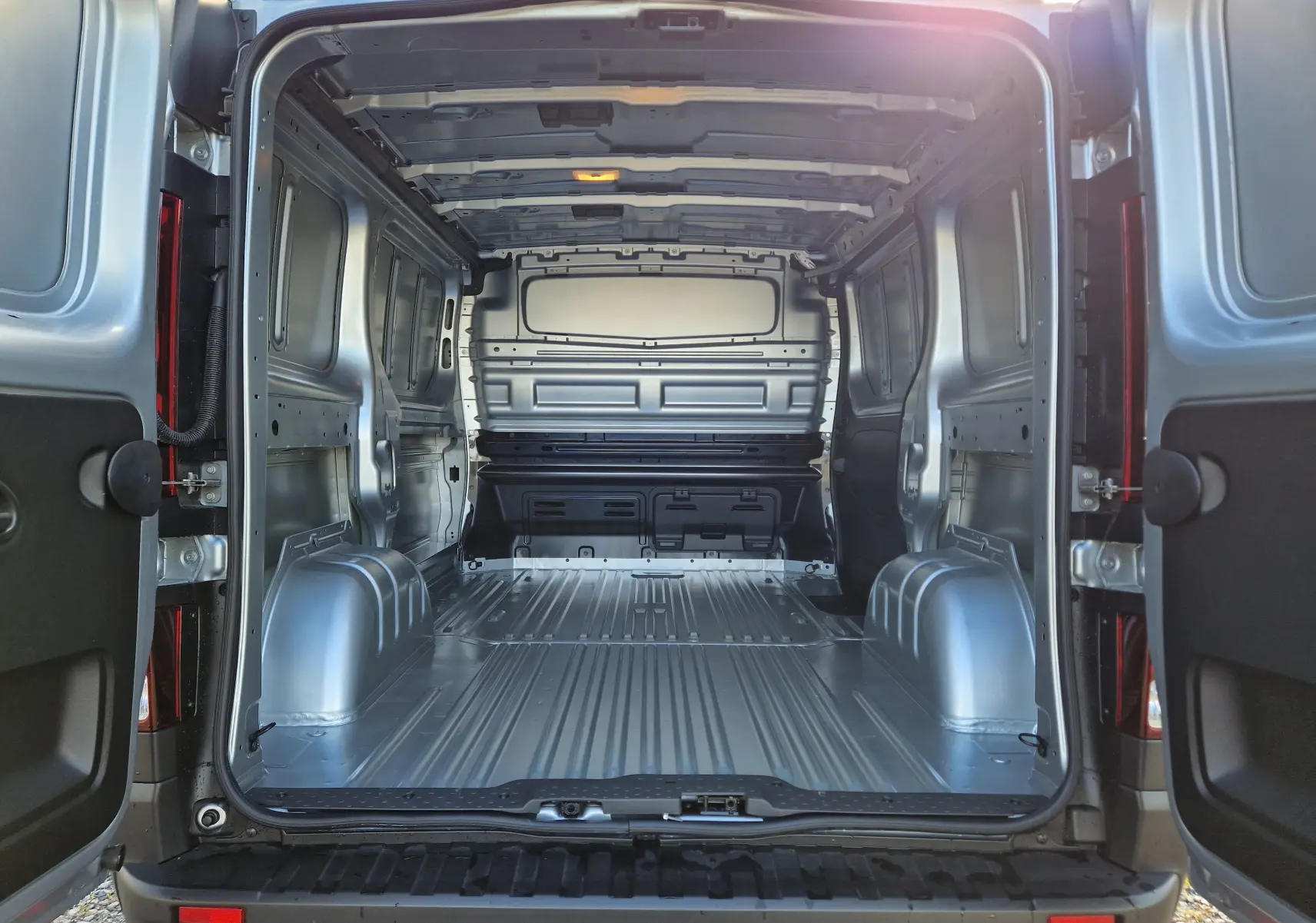 Vue arrière ouverte du Renault Trafic Fourgon gris Highland 2025, montrant l’espace de chargement métallique vide.