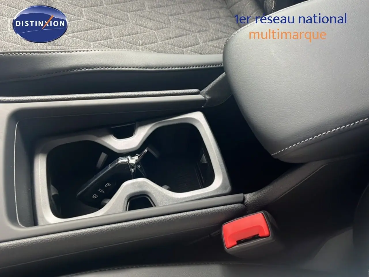 Gros plan intérieur sur le porte-gobelets central avec clé VW, sellerie noire et accoudoir en cuir cousu.