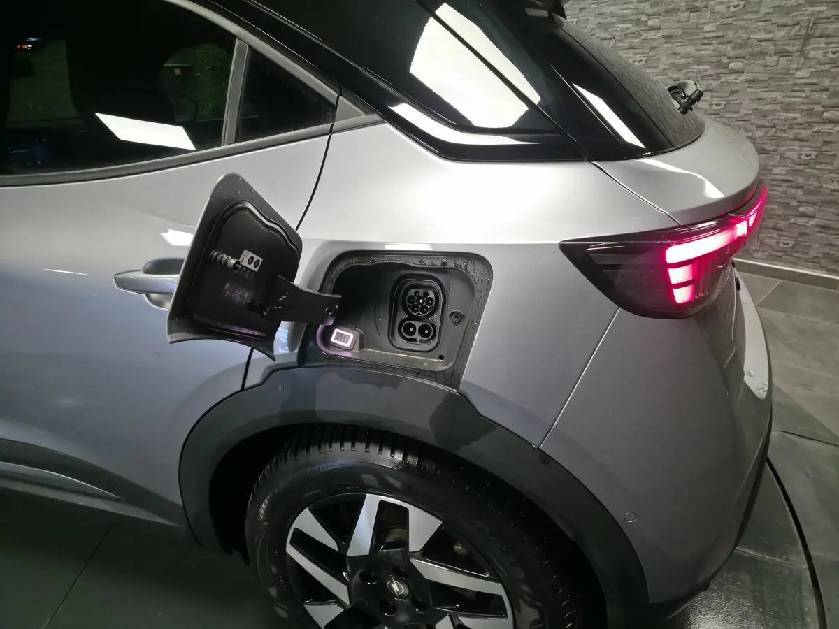 Vue arrière côté gauche d’un Opel Mokka-e gris avec trappe de recharge ouverte et feux arrière LED allumés.