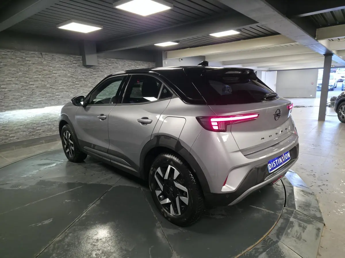Opel Mokka-e gris 3/4 arrière droit, toit noir, jantes alliage diamantées, feux arrière LED allumés.