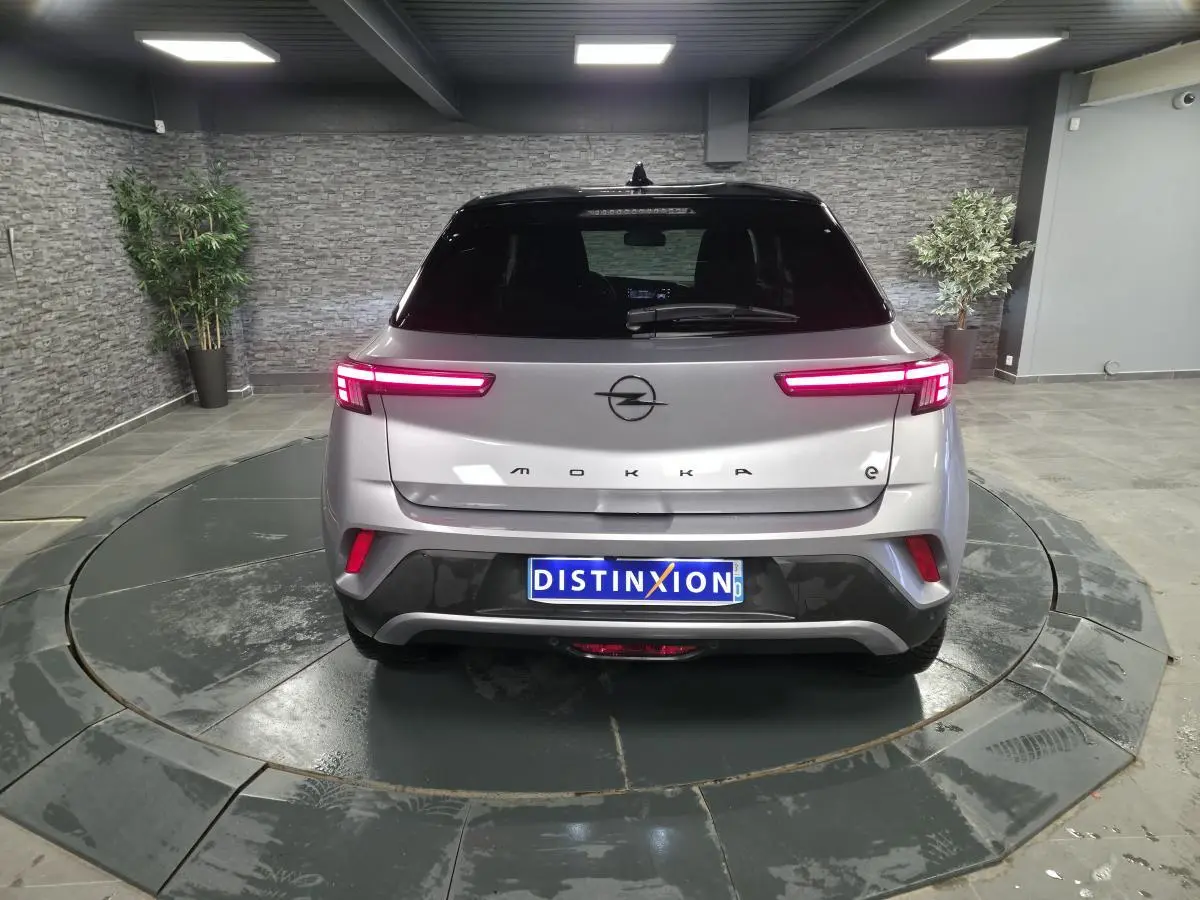 Vue arrière d'un Opel Mokka-e gris 2025 avec feux LED allumés et toit noir dans un showroom.