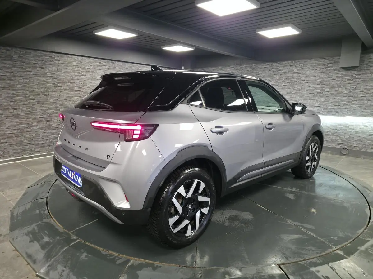 Opel Mokka-e gris 3/4 arrière droit, toit noir, jantes alliage diamantées 17 pouces, feux arrière LED allumés.