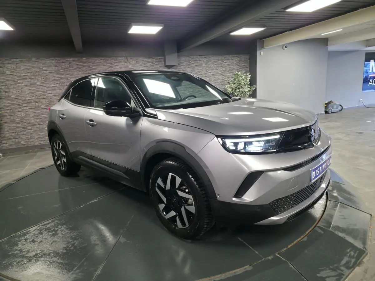 Opel Mokka-e gris 3/4 avant droit avec jantes alliage diamantées et toit noir en intérieur showroom.