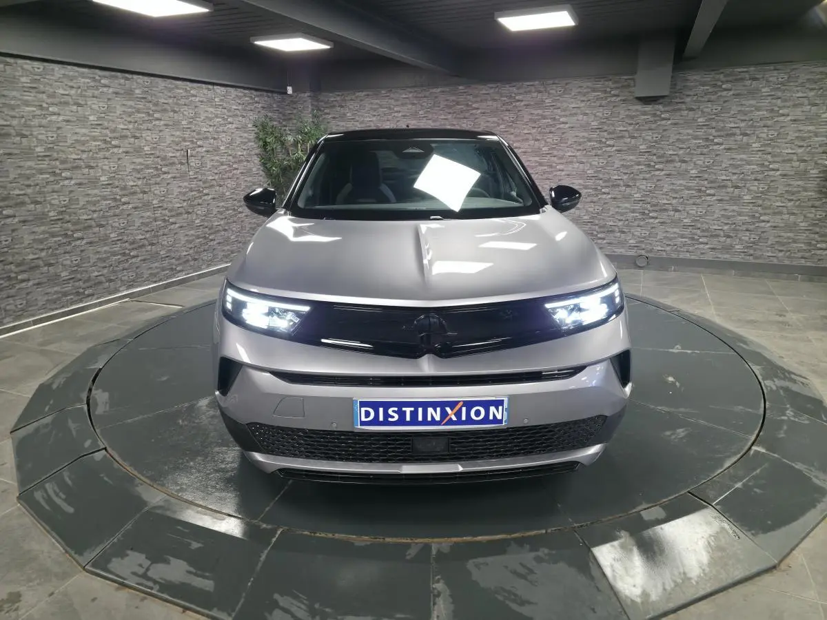 Opel Mokka-e gris vue de face en intérieur, avec phares Matrix LED allumés et calandre noire brillante.