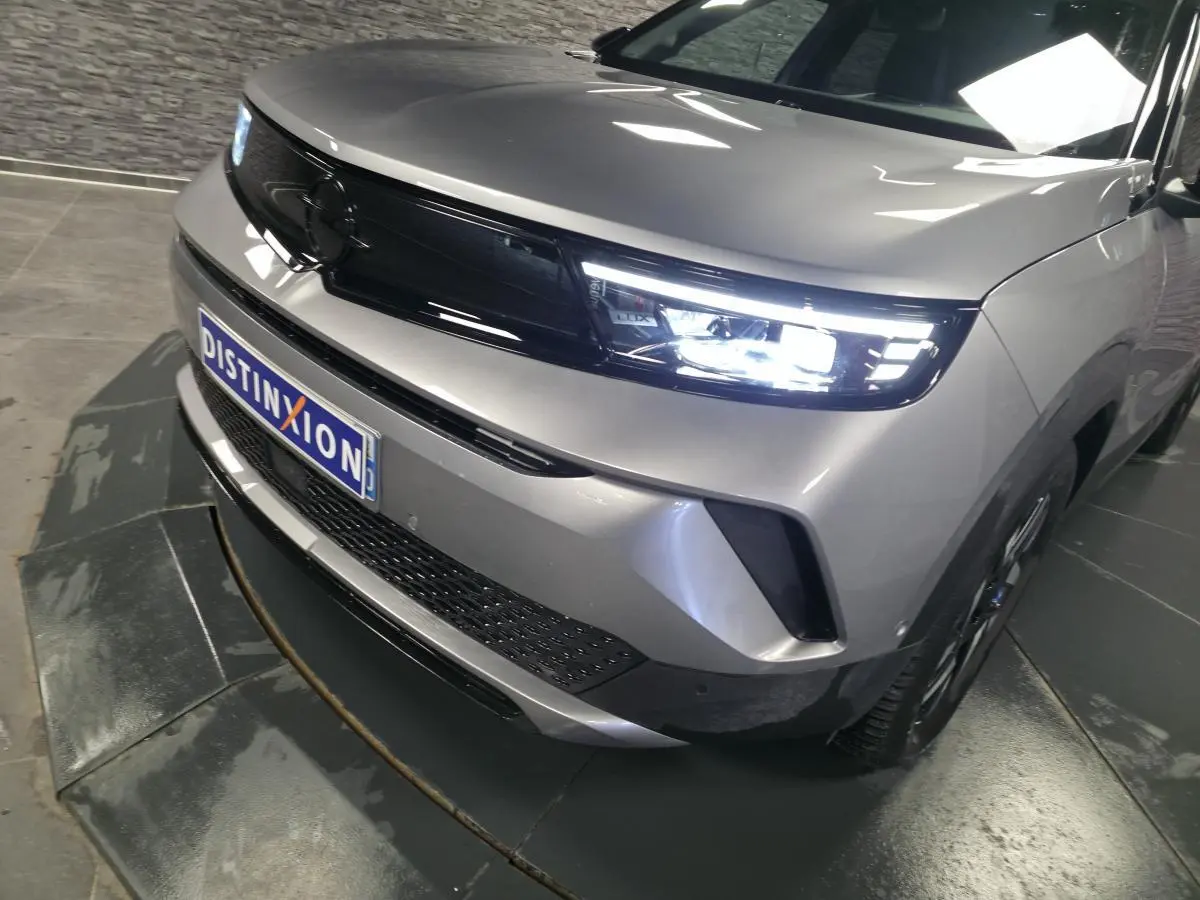Vue 3/4 avant droit de l'Opel Mokka-e gris métallisé avec calandre noire et phares Matrix LED allumés.