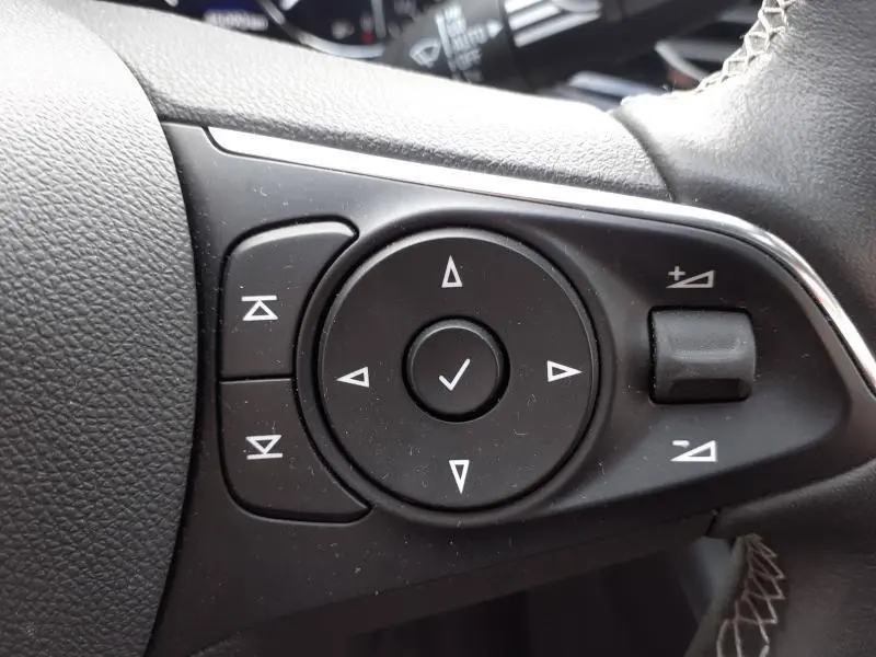 Gros plan sur les commandes noires multifonctions au volant cuir de l'Opel Insignia Grand Sport blanc Glacier.