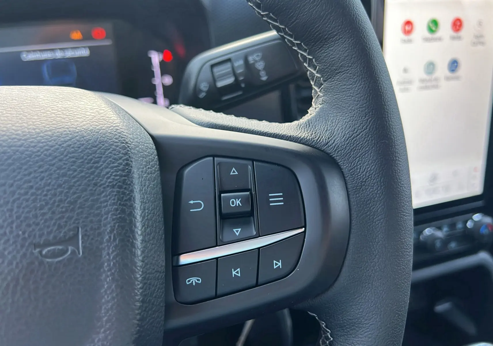 Gros plan sur les commandes au volant du Ford Ranger 2025 noir shadow, avec écran tactile en arrière-plan.