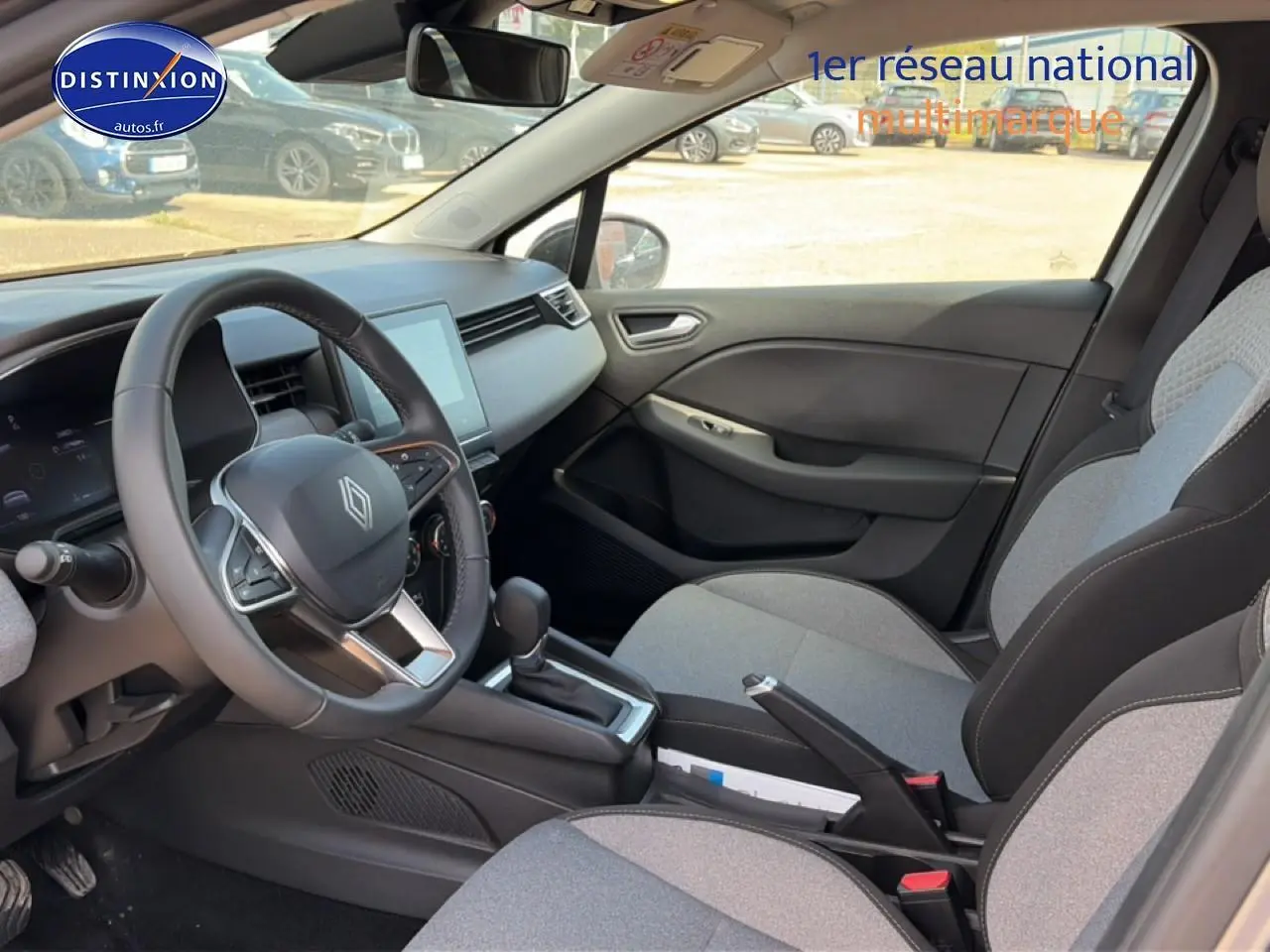 Vue intérieure côté conducteur de la Renault Clio V 1.0 TCe 90 gris métal avec volant multifonction et sièges tissu gris.