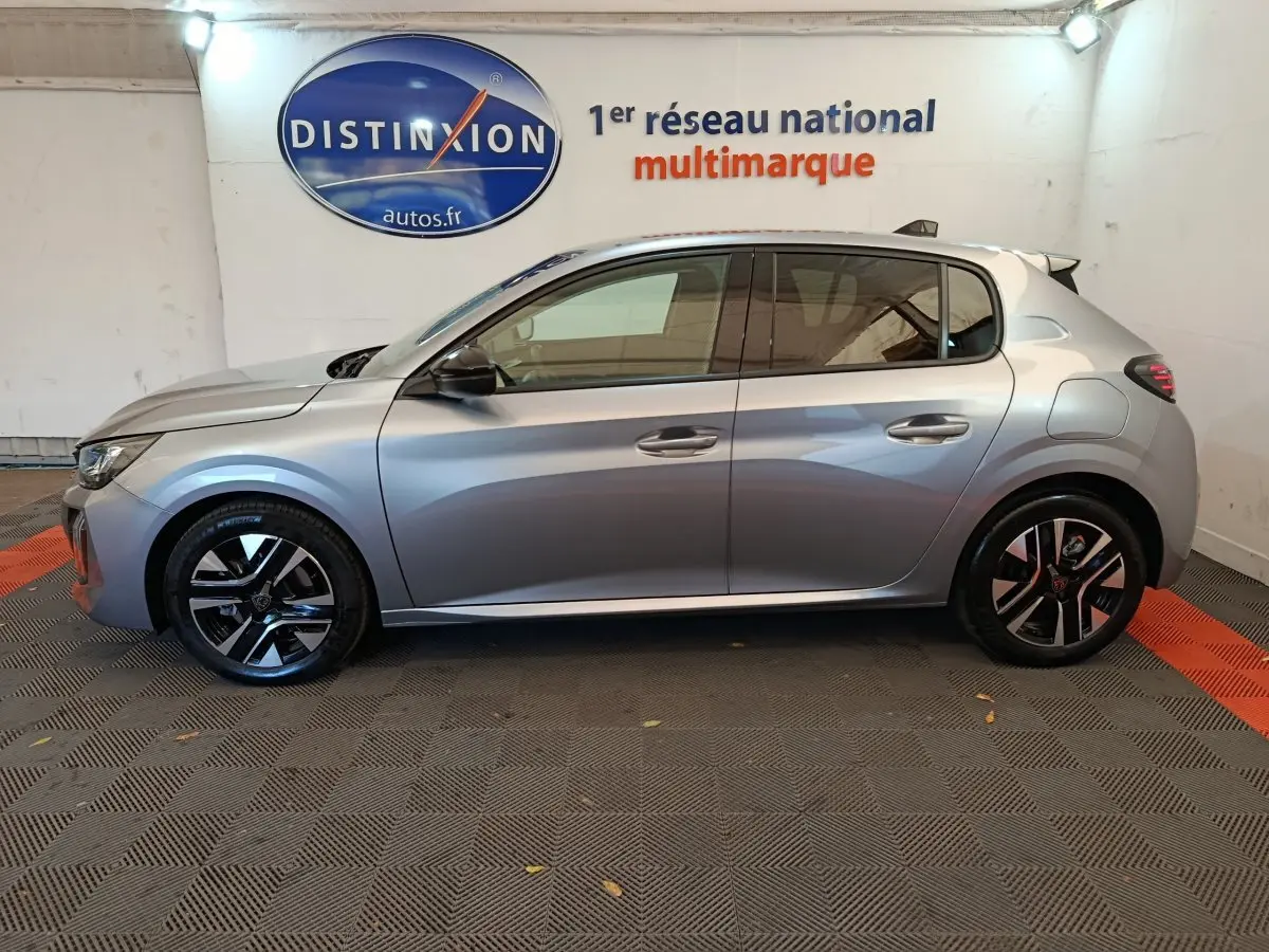 Profil côté gauche d'une Peugeot 208 gris clair 2025, avec jantes noires et détails modernes en intérieur d'exposition.