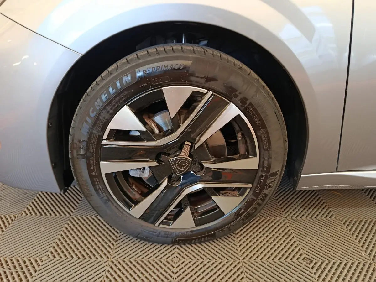 Gros plan sur la roue avant gauche d’une Peugeot 208 gris clair, avec jante alliage noire et argentée.