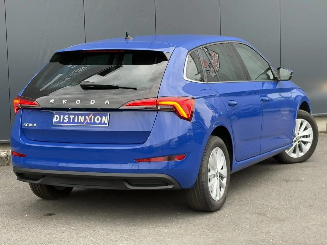 Vue 3/4 arrière droite d'une Skoda Scala 2024 bleu Energy avec feux arrière allumés et jantes alliage argent.