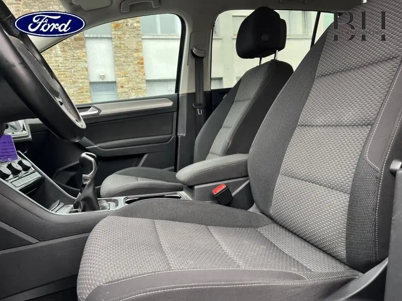 Intérieur avant côté conducteur d'un Volkswagen Touran 2.0 TDI noir, sièges tissu gris et volant cuir multifonction.