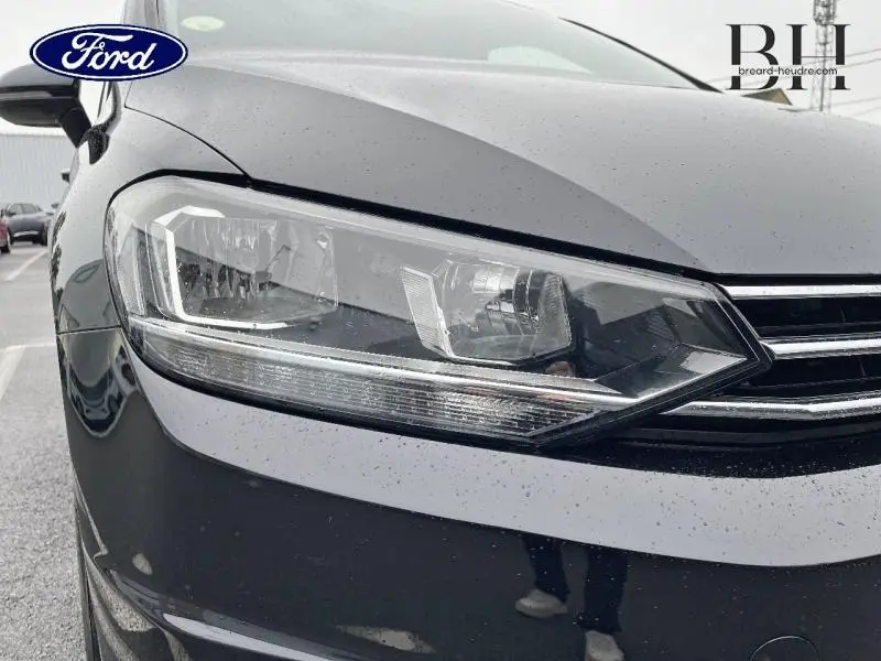 Gros plan sur le phare avant gauche du Volkswagen Touran noir intense nacré, soulignant la calandre chromée et les détails lumineux.