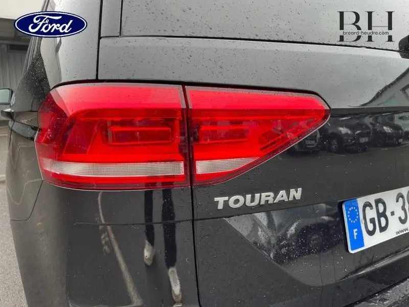 Gros plan sur le feu arrière droit d'un Volkswagen Touran noir intense nacré avec logo et plaque d'immatriculation française visible.
