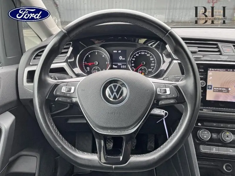 Vue rapprochée du volant cuir multifonction noir du Volkswagen Touran 2021 avec tableau de bord et écran tactile visibles.